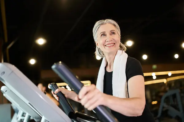 Attractive jolly mature sportswoman in black t shirt exercising actively on elliptical trainer — Stock Photo