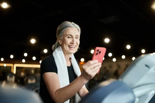 Jolly pretty senior sportswoman with gray hair having video call while training on treadmill in gym — Stock Photo