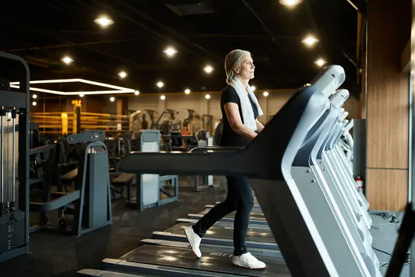 Привлекательная спортивная старшая женщина в спортивной одежде активно тренирующаяся на беговой дорожке пока в тренажерном зале — стоковое фото