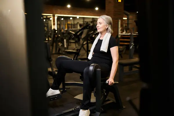 Schöne ältere fröhliche Sportlerin mit grauen Haaren und Handtuch beim Training auf dem Wadengerät im Fitnessstudio — Stockfoto