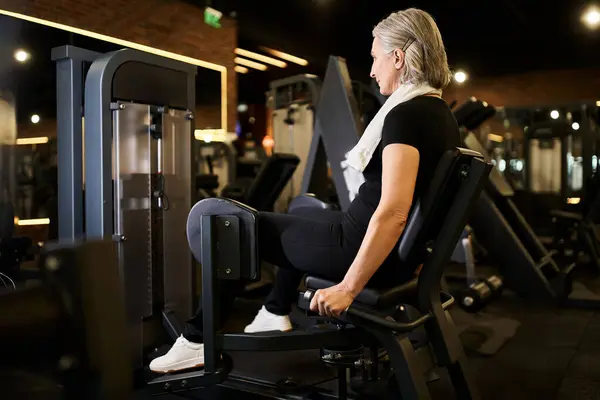 Attraente donna positiva matura in allenamento abbigliamento sportivo attivamente sulla macchina del polpaccio mentre in palestra — Foto stock