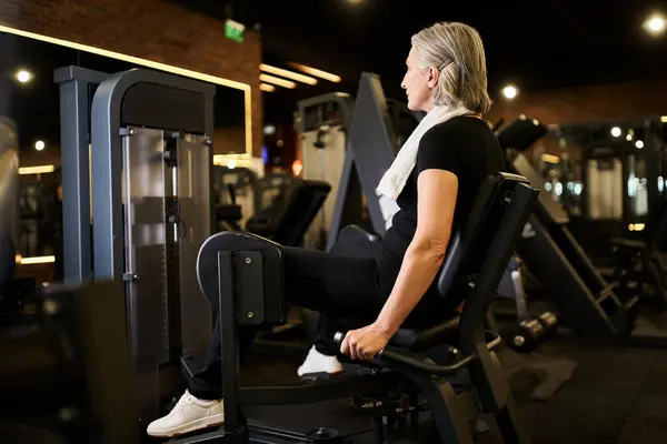 Atractiva mujer mayor de pelo gris en traje deportivo ejercitando activamente en la máquina de becerro en el gimnasio - foto de stock
