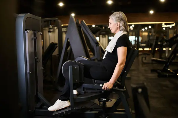 Boa aparência atlética mulher sênior no treinamento sportswear ativamente na máquina de bezerro enquanto no ginásio — Fotografia de Stock