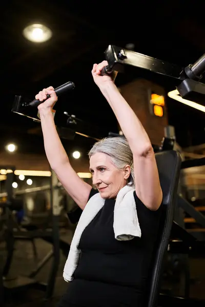 Appealing athletic senior woman in sportswear with gray hair exercising on chest press machine — Stock Photo