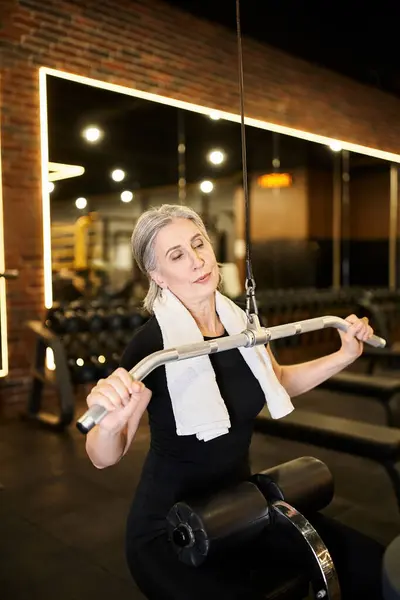 Pretty athletic senior woman in cozy outfit exercising actively with lats pulldown machine in gym — Stock Photo