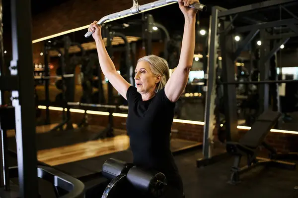 Atractiva mujer mayor deportivo en traje acogedor ejercicio activo con lats máquina de extracción en el gimnasio - foto de stock