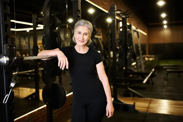 Cheerful appealing senior woman with gray hair in sportswear posing and smiling at camera in gym — Stock Photo