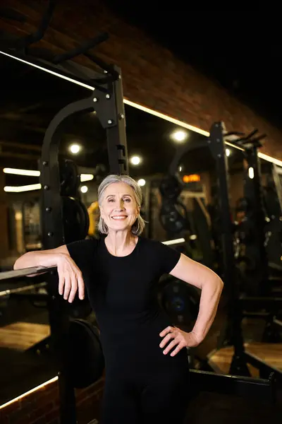Joyous appealing mature woman with gray hair in sportswear posing and smiling at camera in gym — Stock Photo