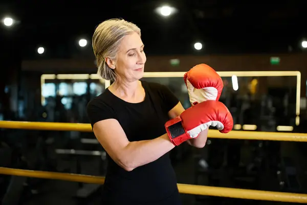 Appealing jolly mature woman in sportswear with gray hair and boxing gloves posing on ring in gym — Stock Photo