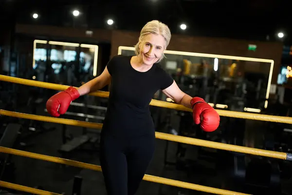 Good looking jolly mature sportswoman with boxing gloves smiling at camera while on ring in gym — Stock Photo