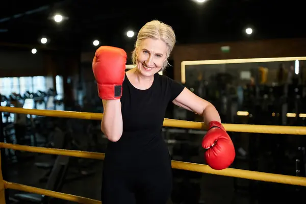 Beautiful cheerful senior sportswoman with boxing gloves smiling at camera while on ring in gym — Stock Photo