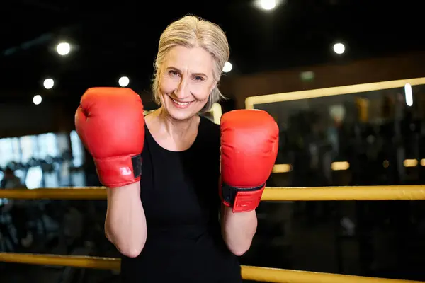 Bella donna anziana atletica allegra con i guanti da boxe sorridente alla macchina fotografica mentre sul ring in palestra — Foto stock