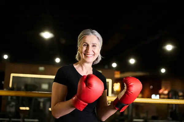 Appealing jolly mature woman in sportswear with boxing gloves training on ring and smiling at camera — Stock Photo