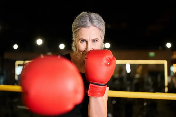 Bella donna anziana allegra in abbigliamento sportivo con guanti da boxe formazione sul ring e sorridente alla macchina fotografica — Foto stock