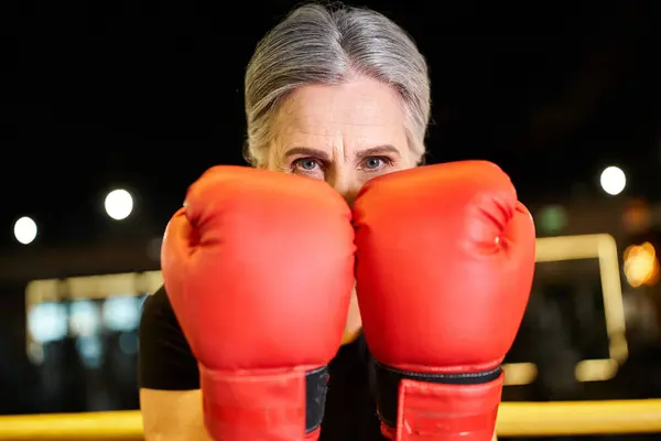 Pretty joyous mature woman in sportswear with boxing gloves training on ring and smiling at camera — Stock Photo
