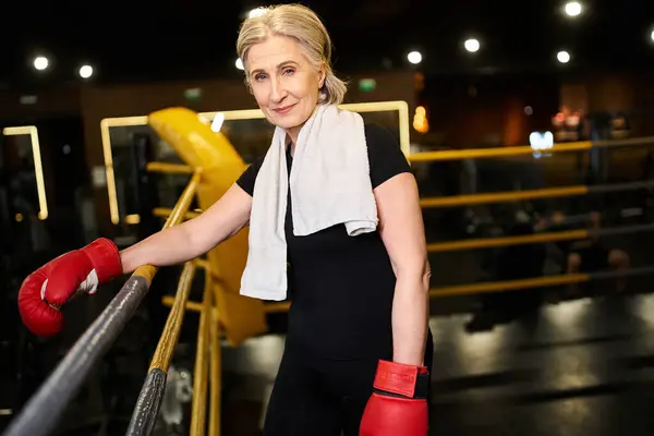 Привлекательная старшая спортсменка с полотенцами и боксёрскими перчатками, улыбающаяся в камеру на ринге — стоковое фото
