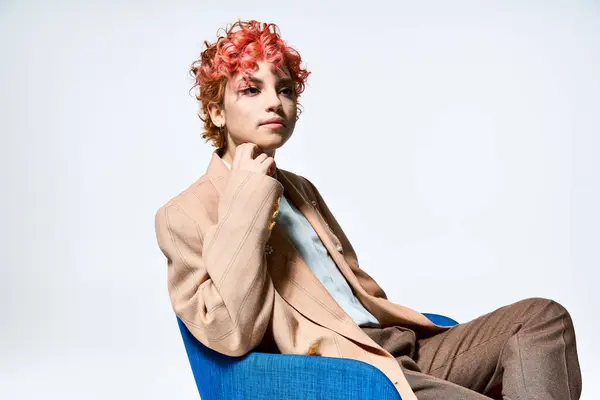 Une femme aux cheveux roux, vêtue de façon extravagante, assise sur une chaise bleue. — Photo de stock