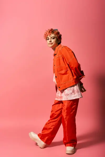 Femme extraordinaire vêtue d'une veste orange et pantalon rouge se distingue sur un fond vibrant. — Photo de stock