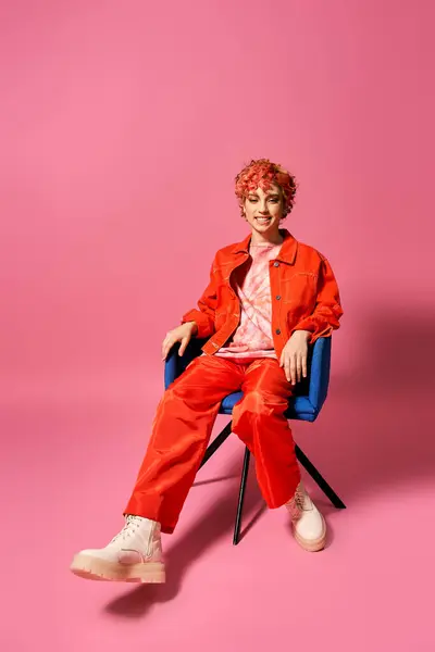 Extraordinary woman seated in a chair against a vibrant pink background. — Stock Photo