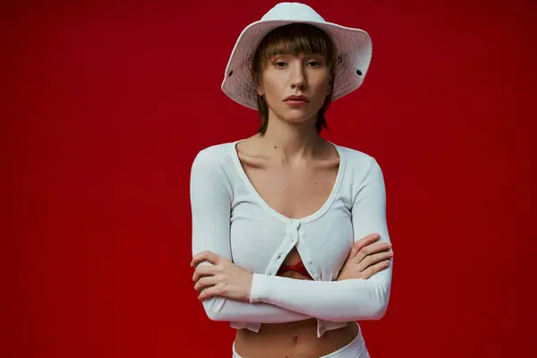 A young woman in a white hat and shirt exudes elegance against a vibrant red backdrop. — Stock Photo