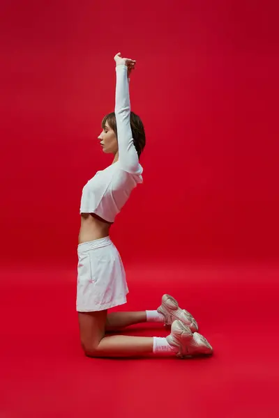 Femme élégante en tenue blanche effectuant gracieusement le yoga sur un fond rouge vibrant. — Photo de stock