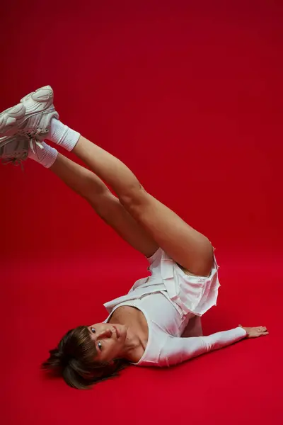 Young woman in white sportswear performs yoga on vibrant red background. — Stock Photo