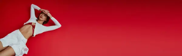 Elegant young woman in white smart sportswear with red tie on vibrant red backdrop. — Stock Photo