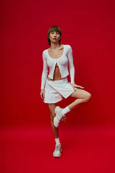 Una mujer con estilo en una falda corta y la parte superior posando con gracia sobre un vibrante telón de fondo rojo. - foto de stock