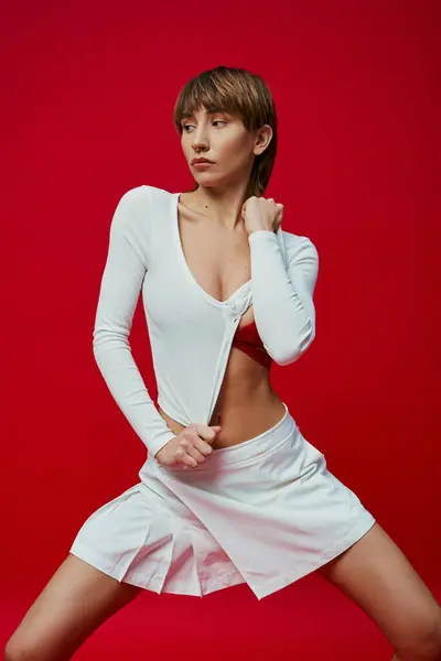 A stylish young woman in a short skirt strikes a pose against a vibrant red backdrop. — Stock Photo