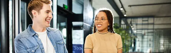 Um homem e uma mulher multicultural em traje casual ficam ao lado um do outro em um lobby do hotel durante uma viagem corporativa. — Fotografia de Stock