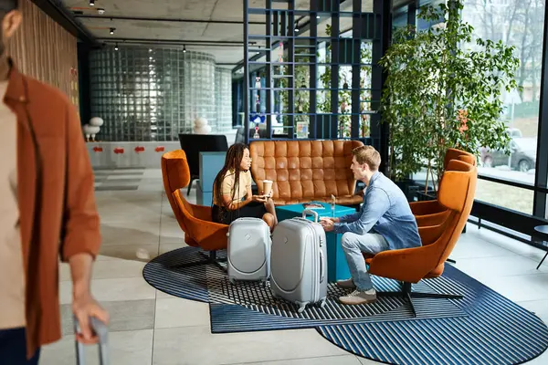 Multicultural man and woman sitting on a couch, wearing casual clothes, in a hotel lobby during a corporate trip. — Stock Photo