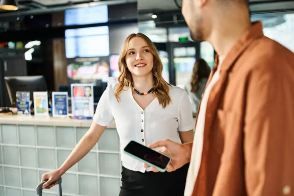 A woman stands in front of a man holding a smartphone in a hotel lobby during a corporate trip. — Stock Photo