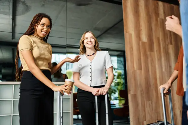 Two women in casual clothes stand with luggage, smiling in a hotel lobby during a corporate trip. — Stock Photo
