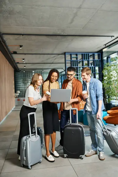 Multicultural colleagues in hotel lobby, discussing travel plans around a laptop with luggage. — Stock Photo