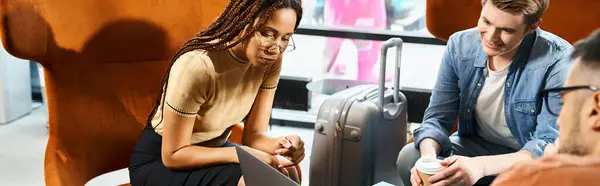 Multicultural colleagues in casual clothes discussing travel plans around a table with luggage in a hotel lobby. — Stock Photo