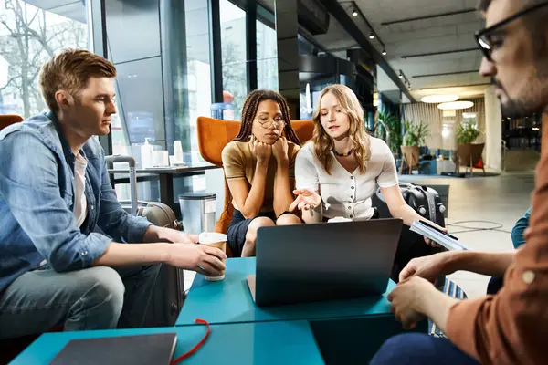 Multicultural business colleagues in casual attire work on laptop and collaborate around a table in a cozy setting. — Stock Photo
