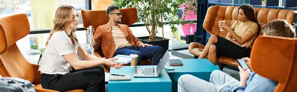 Multicultural colleagues in casual attire sit in chairs in a hotel lobby during a corporate trip. — Stock Photo