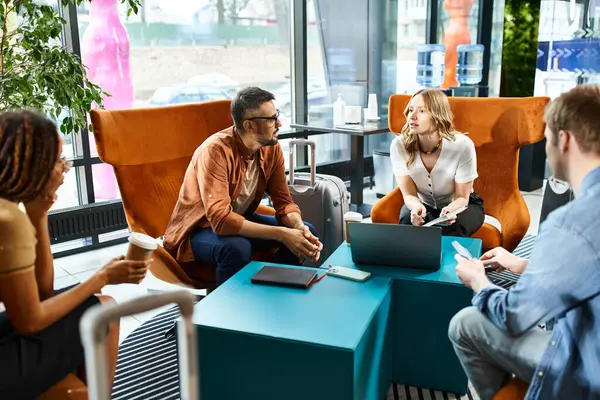 Colegas multiculturais em traje casual absorvidos no trabalho em laptops em torno de uma mesa em um lobby vibrante hotel. — Fotografia de Stock