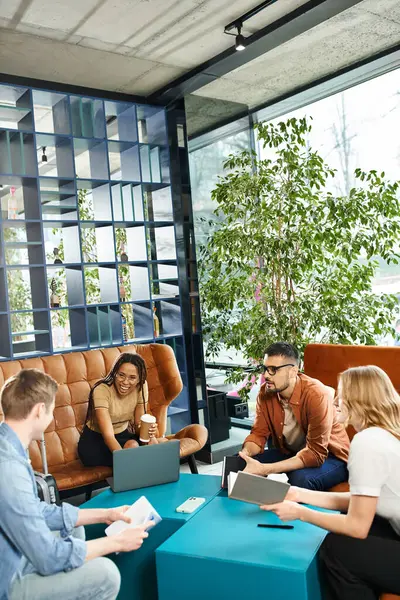 Multicultural colleagues in casual attire gathered around a table with laptop for a productive work session. — Stock Photo