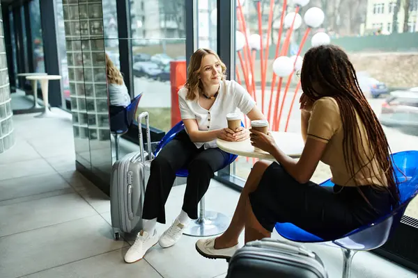 Dos empresarias diversas están sentadas en sillas, compartiendo una conversación durante un viaje corporativo. - foto de stock