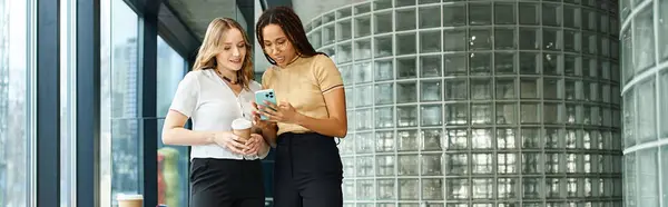 Zwei multikulturelle Kollegen stehen zusammen, vertieft in einen gemeinsamen Moment, während sie auf ein Handy schauen.. — Stockfoto
