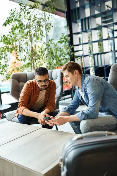 Two multicultural colleagues, diverse businesspeople, sitting on a couch, engrossed in a cell phone. — Stock Photo