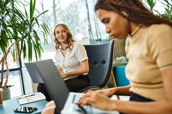 Due donne con computer portatili che lavorano insieme a un tavolo in un moderno spazio di coworking, impegnate in una riunione del team di startup. — Foto stock