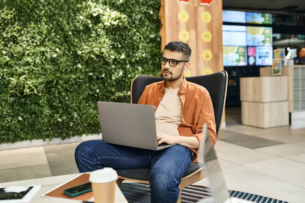 A man in a chair, engrossed in his laptop, surrounded by the buzz of a coworking space where startup team members collaborate. — Stock Photo