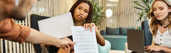 Dos mujeres, colegas en un moderno espacio de coworking, están sentadas en una mesa, absortas en documentos y papeles. - foto de stock