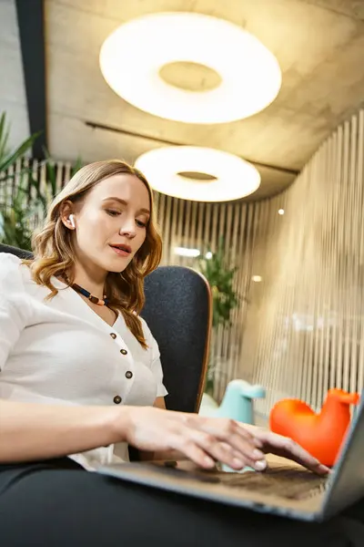 Uma mulher imersa no trabalho, sentada em uma cadeira usando um computador portátil em um espaço de co-trabalho moderno. — Fotografia de Stock