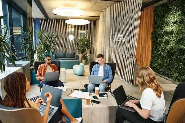 Um grupo diversificado de profissionais se senta em torno de uma mesa, absorvido em seus laptops, colaborando em um projeto de startup. — Fotografia de Stock