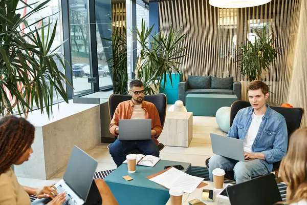 A diverse group of colleagues sitting around a table with laptops, collaborating on projects in a modern coworking space. — Stock Photo