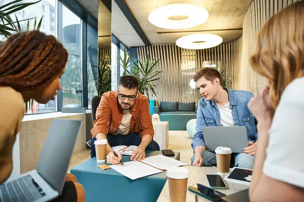 A diverse group of individuals working together around a table with laptops in a modern business setting. — Stock Photo