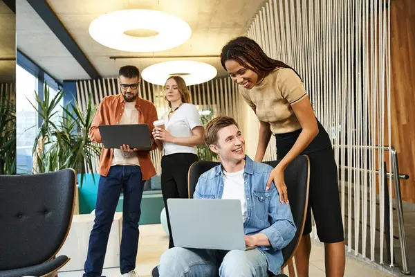 A team of colleagues surrounds a man on a laptop, collaborating on a project in a modern coworking space. — Stock Photo